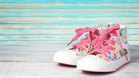 Bunte Sneaker mit rosa Schnürsenkeln stehen auf einem hellen Holzuntergrund vor einer pastellfarbenen Wand.