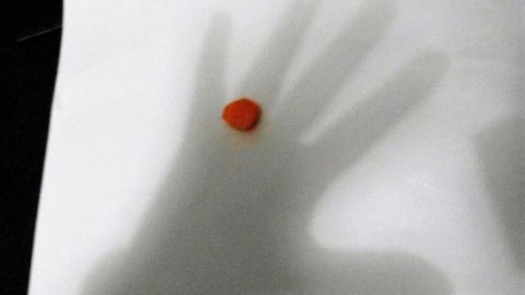 Eine Hand zeichnet ihren Schatten auf ein Blatt Papier, während ein kleiner roter Punkt in der Mitte sichtbar ist.