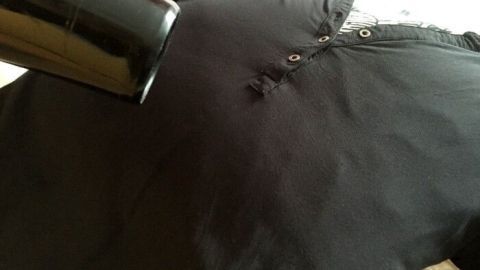 Ein schwarzes Hemd liegt flach, während ein Haartrockner direkt darauf gerichtet ist, um es ohne Bügeleisen zu glätten.