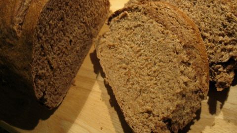Vollkornbrot liegt auf einem Holzbrett, ein paar Scheiben sind geschnitten, um die dichte Textur zu zeigen.