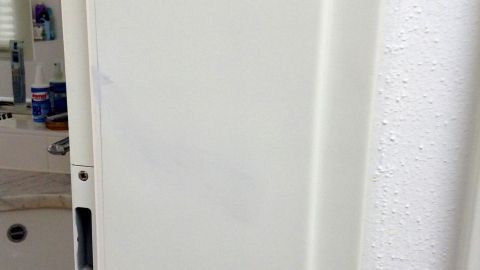 Eine Badezimmertür mit dunkler Haarfarbe, die teilweise entfernt wurde, steht in einem hellen Raum mit einem Waschbecken im Hintergrund.