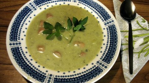 Eine grüne Giersch-Kartoffel-Cremesuppe in einer Schale, garniert mit frischen Kräutern, steht auf einem Holztisch.