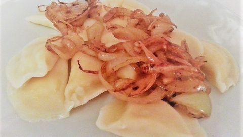 Piroggen liegen appetitlich auf einem weißen Teller, garniert mit goldbraunen, knusprigen Zwiebeln.