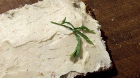 Ein Stück Quarkbrot liegt auf einem Holzbrett, bestrichen mit Quark und garniert mit einem frischen Kräuterzweig.