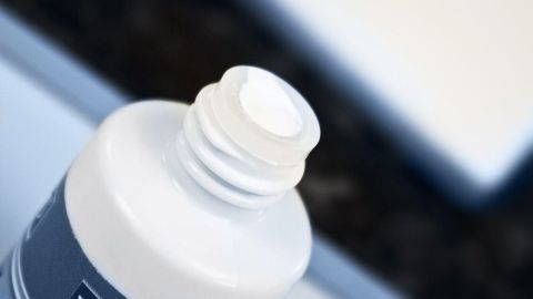 Eine Flasche Tipp-Ex wird geöffnet, während eine Hand einen Pinsel aus dem Deckel hebt, um die Flüssigkeit zu verwenden.