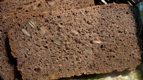 Dunkles Roggen-Dinkel-Vollkornbrot mit Kernen liegt auf einem bunten Tuch und zeigt eine rustikale Textur und Färbung.