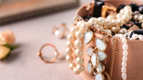 Eine Schmuckschatulle mit Vintage-Schmuck und Perlen liegt auf einem Tisch, umgeben von soften Blumen und einem Spiegel.