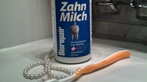 Eine Flasche Zahnmilch steht auf einem Waschbecken, daneben liegt eine Zahnbürste – beides für gesunde Zähne.