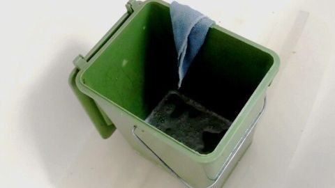 Ein grüner Eimer steht leer in einem hellen Raum, bereit für den Frühjahrsputz, mit einem blauen Tuch am Rand.