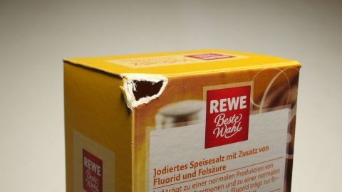 Das Salzpäckchen wird vorsichtig geöffnet, um den Inhalt herauszufüllen, während der Hintergrund neutral gehalten ist.