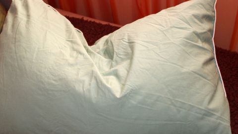 Die Schmerzen gehen davon zwar nicht weg, aber es lindert das Ganze etwas.. Eine zerknitterte Kissenhülle liegt auf einem dunklen Untergrund, umgeben von orangefarbenem Stoff, was eine gemütliche Atmosphäre erzeugt.