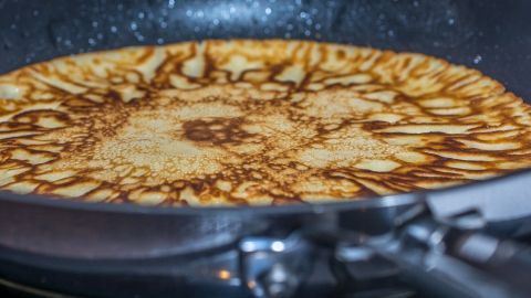 In einer Pfanne brät ein goldbrauner Pfannkuchen, umgeben von einer leicht glänzenden, heißen Oberfläche.