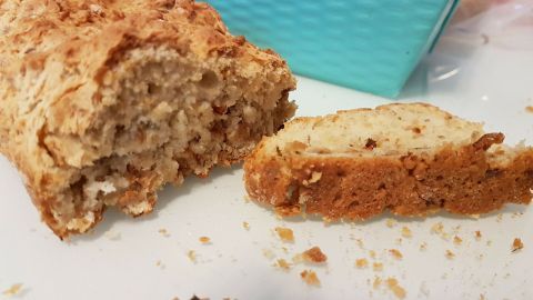 Ein frisches Zwiebelbrot liegt auf einem weißen Teller, neben einem Stück, das gerade abgeschnitten wurde, umgeben von Krümeln.