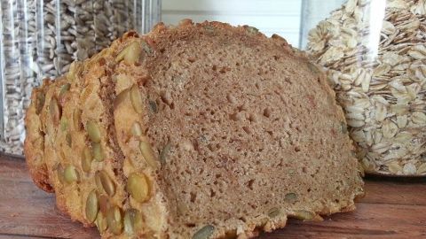 Ein Laib Dinkelbrot steht auf einem Tisch, umgeben von Glasbehältern mit Getreide. Es wirkt frisch und einladend.