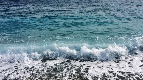 Sanfte Wellen rollen an einen Kiesstrand, während das klare Wasser unter einem bewölkten Himmel plätschert.