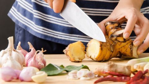 Hände schneiden frischen Ingwer und Knoblauch auf einem Holzbrett, um Gerüche zu entfernen und natürliche Hausmittel zu verwenden.