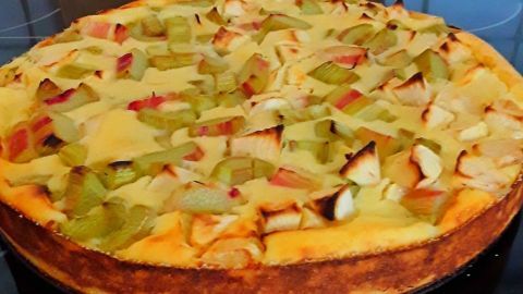 Ein Käsekuchen ohne Boden mit Rhabarberstücken ist frisch aus dem Ofen. Er steht auf einer Arbeitsfläche in einer modernen Küche.