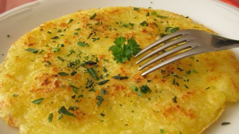 Goldbraune Kartoffelbratlinge liegen auf einem weißen Teller, garniert mit frischen Kräutern und einer Gabel daneben.