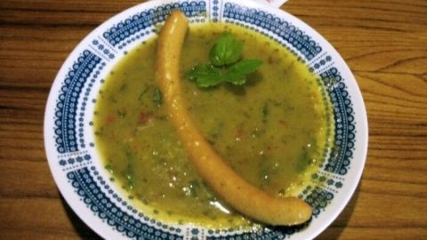 Eine bunte Gurken-Kartoffel-Suppe in einer schönen Schüssel, garniert mit einer Banane und frischem Koriander auf einem Holztisch.