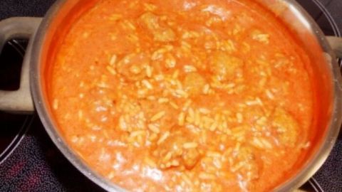 Ein Topf mit Tomatensuppe, der auf dem Herd steht, enthält Reis und Hackbällchen in einer leuchtend roten Sauce.