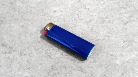 Ein blaues Gasfeuerzeug liegt auf einer hellen, strukturierten Oberfläche und wartet darauf, nachgefüllt zu werden.