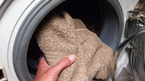 Eine Hand hält ein Handtuch, das in einer offenen Waschmaschine liegt. Es scheint, als ob ein Teil vergessen wurde.