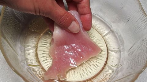 Fleisch ohne Tiefkühler aufbewahren: Man nehme ein Glasgefäß, fülle es halb mit einem günstigen Speiseöl, lege die Fleischstücke hinein und ab in den Kühlschrank. Eine Hand hält ein Stück Fleisch über eine Schüssel, in der es mariniert oder vorbereitet wird, ohne tiefgekühlt zu sein.