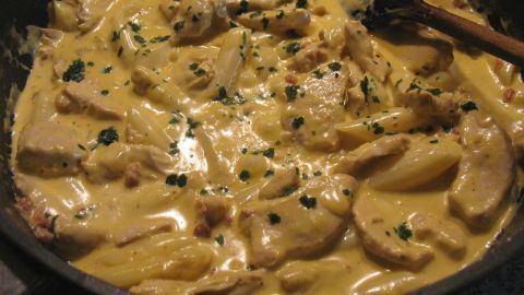 Saftige Hähnchenstücke in einer cremigen Sahnesauce werden in einer Pfanne mit Gewürzen und Kräutern zubereitet.
