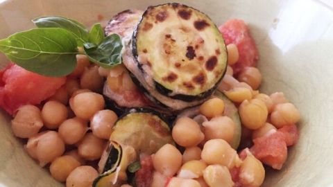 Ein bunter Kichererbsensalat mit gegrilltem Gemüse und frischen Kräutern in einer Schale, serviert auf einem Tisch.