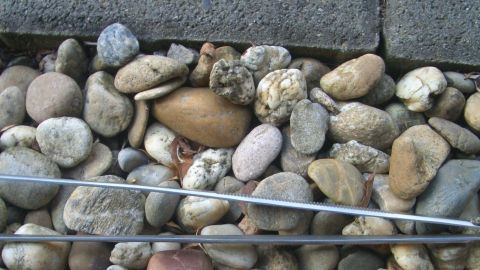 Kieselsteine liegen auf dem Boden, während ein Werkzeug darüber bewegt wird, um Laub zu entfernen und die Steine zu reinigen.