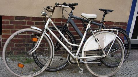 Ein Fahrrad steht geparkt auf einem Gehweg, bereit für die Saison, neben einem weiteren Rad in einer urbanen Umgebung.