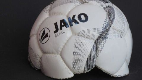 Ein alter Fußball liegt auf einem schwarzen Hintergrund und zeigt Gebrauchsspuren, was Möglichkeiten zur Wiederverwendung anregt.