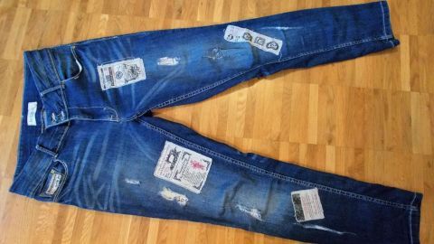 Eine blaue Jeans liegt flach auf einem Holzfußboden und zeigt kreative Aufkleber zur Individualisierung.