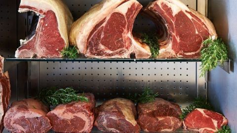 Reife Rindersteaks liegen in mehreren Reihen auf Regalen, umgeben von frischem Grün, zur optimalen Dry Aging-Präsenz.