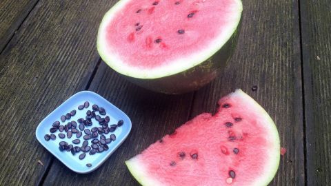 Saftige Wassermelonenhälften liegen auf einem Holztisch, daneben eine Schale mit gerösteten Melonenkerne.