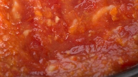 Ein silberner Löffel rührt in einer dicken, roten Tomatensauce in einem Gefrierbehälter, bereit zum Portionieren.