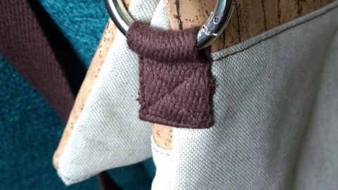 Ein Ringkarabiner hält an einer Umhängetasche, die auf einem blauen Sofa platziert ist, für Stabilität und Stil.