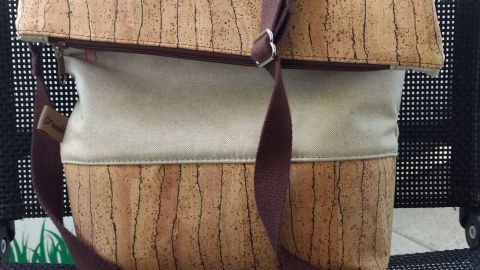 Eine FoldOver-Tasche aus Dekostoff und Korkleder steht auf einem schwarzen Stuhl, mit braunem Tragegurt und einem gefalteten Deckel.