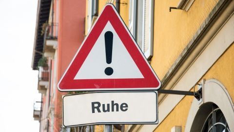Ein Verkehrsschild warnt vor Lärm und fordert zur Ruhe auf, platziert an einer farbigen Hauswand in einer urbanen Umgebung.