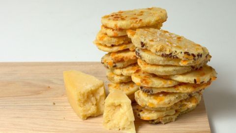 Käsewölkchen liegen auf einem Holzbrett, während sie appetitlich gestapelt sind und ein Stück Käse daneben liegt.
