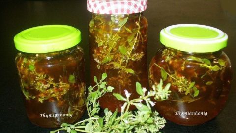 Gläser mit Thymianhonig stehen auf einem Tisch, umgeben von frischen Thymianzweigen, die appetitlich wirken.