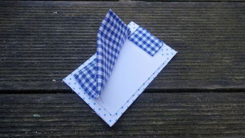 Eine Einladungskarte für eine Übernachtungsparty liegt auf einem Holzuntergrund, das blaue Karomuster zieht die Blicke an.