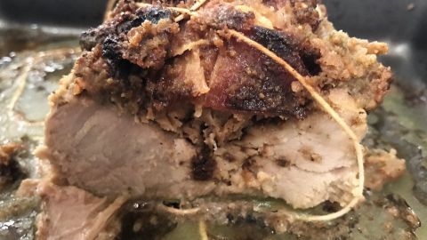 Gebackenes Schweinefilet mit einer knusprigen, gefüllten Kruste wird in einer Backform präsentiert, umgeben von Bratensaft.
