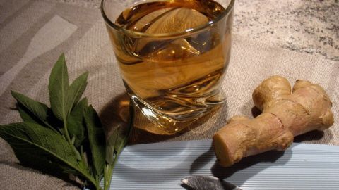 Ein Glas Salbei-Ingwer-Tee steht neben frischem Ingwer und geschnittenen Ingwerstücken auf einem Holzschneidebrett.