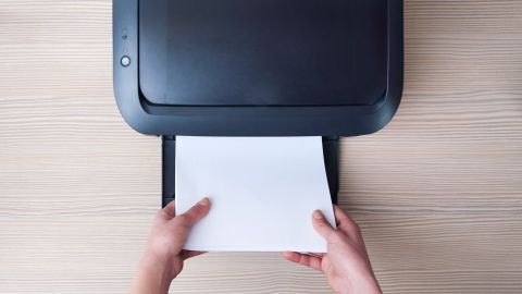 Ein Drucker wird verwendet, um ein Blatt Papier einzuziehen, während Hände es an die Vorderseite halten.