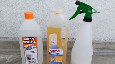 Zwei Flaschen mit Reinigungsmitteln und eine Sprühflasche stehen auf einem glatten Untergrund, um Blattläuse zu bekämpfen.