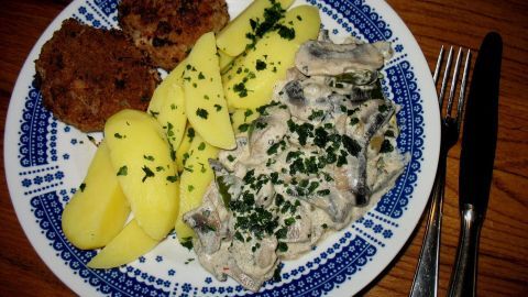 Eine bunte Platte zeigt cremige Sahne-Champignons mit Bratpaprika, umgeben von Kartoffeln und Kroketten, hübsch garniert.