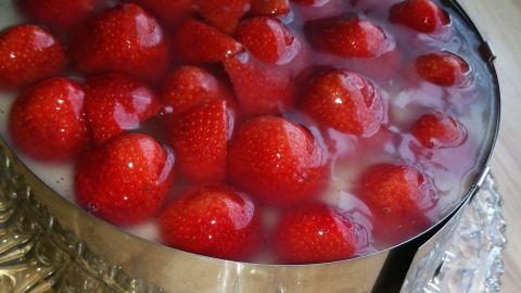 Ein reicher Tortenguss aus Kartoffelmehl bedeckt die frischen Erdbeeren in einer runden Form auf einem gläsernen Teller.