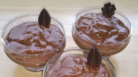 Schokoladenpudding in drei Schalen sitzt auf einer Holzoberfläche und wird von Schokoladenblättern dekoriert.