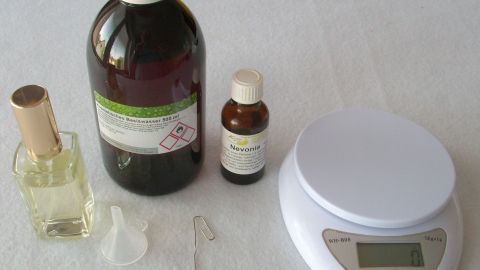 Eine Flasche mit Flüssigkeit steht neben ätherischen Ölen und einer digitalen Waage auf einem weißen Tisch, bereit zum DIY Eau de Parfum.